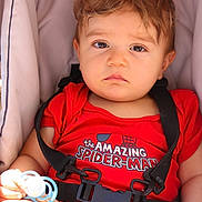 Milann participe au concours pour gagner de l'argent avec cette photo : baby, child, car_seat, red_clothing, pacifier, straps, serious_expression, indoors, cushion, infant, person, young_child, seatbelt, onesie, head, face, hand, light, comfort, casual