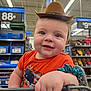 baby, blue_scrunchie, child, cowboy_hat, cute, hand, happy, indoor, infant, orange_shirt, person, portrait, price_tags, retail, shelves, shopping, shopping_cart, smiling, store_interior, whale_design
