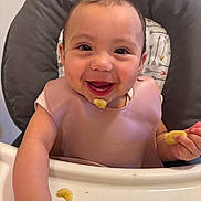 Azaelia-Ray joined the competition — help win amazing prizes! baby, high_chair, bib, food, banana, smile, happy, child, eating, face, hand, cushion, pattern, indoor, person, cute, infant, meal, young_child, cheerful