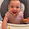 baby, high_chair, bib, food, banana, smile, happy, child, eating, face, hand, cushion, pattern, indoor, person, cute, infant, meal, young_child, cheerful