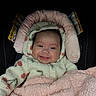 baby, smiling, infant, car_seat, blanket, hooded_jacket, pink, cozy, cute, child, face, warm_clothing, happy, indoors, portrait, soft_texture, warning_label, seat, child_safety, closeup