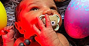 Kamari joined the competition — help win amazing prizes! baby, infant, pacifier, beads, colorful, easter_eggs, decorated_eggs, red_light, hand, face, skin, lying_down, closeup, cute, child, newborn, soft_texture, background, playful, indoors