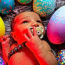 baby, infant, pacifier, beads, colorful, easter_eggs, decorated_eggs, red_light, hand, face, skin, lying_down, closeup, cute, child, newborn, soft_texture, background, playful, indoors