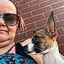 woman, dog, brick_wall, sunglasses, earrings, casual, portrait, pet, outdoor, curious, side_profile, expression, human, animal, closeup, texture, pattern, clothing, skin, head