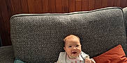 Romy a rejoint le concours — aidez-le/la à gagner de superbes lots ! baby, smiling, couch, pillow, window, indoor, child, happy, bib, clothing, patterned_wallpaper, wood_paneling, natural_light, infant, sitting, face, person, furniture, blanket, home