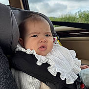 Romy a rejoint le concours — aidez-le/la à gagner de superbes lots ! baby, car_seat, child, infant, white_clothing, frilly_bib, car_interior, seatbelt, window, cloudy_sky, face, portrait, person, expression, young_child, sitting, seat, safety, cozy, curious