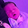 newborn, baby, sleeping, portrait, face, yawning, closed_eyes, mitten, striped_clothing, onesie, infant, indoor, close_up, cuddled, blanket, textile, purple_lighting, phone_screenshot, cozy, peaceful