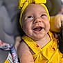baby, child, smiling, yellow_clothing, headband, sunflower_pattern, happy, cute, portrait, infant, skin, hand, face, person, indoors, closeup, expression, joy, holding, seat