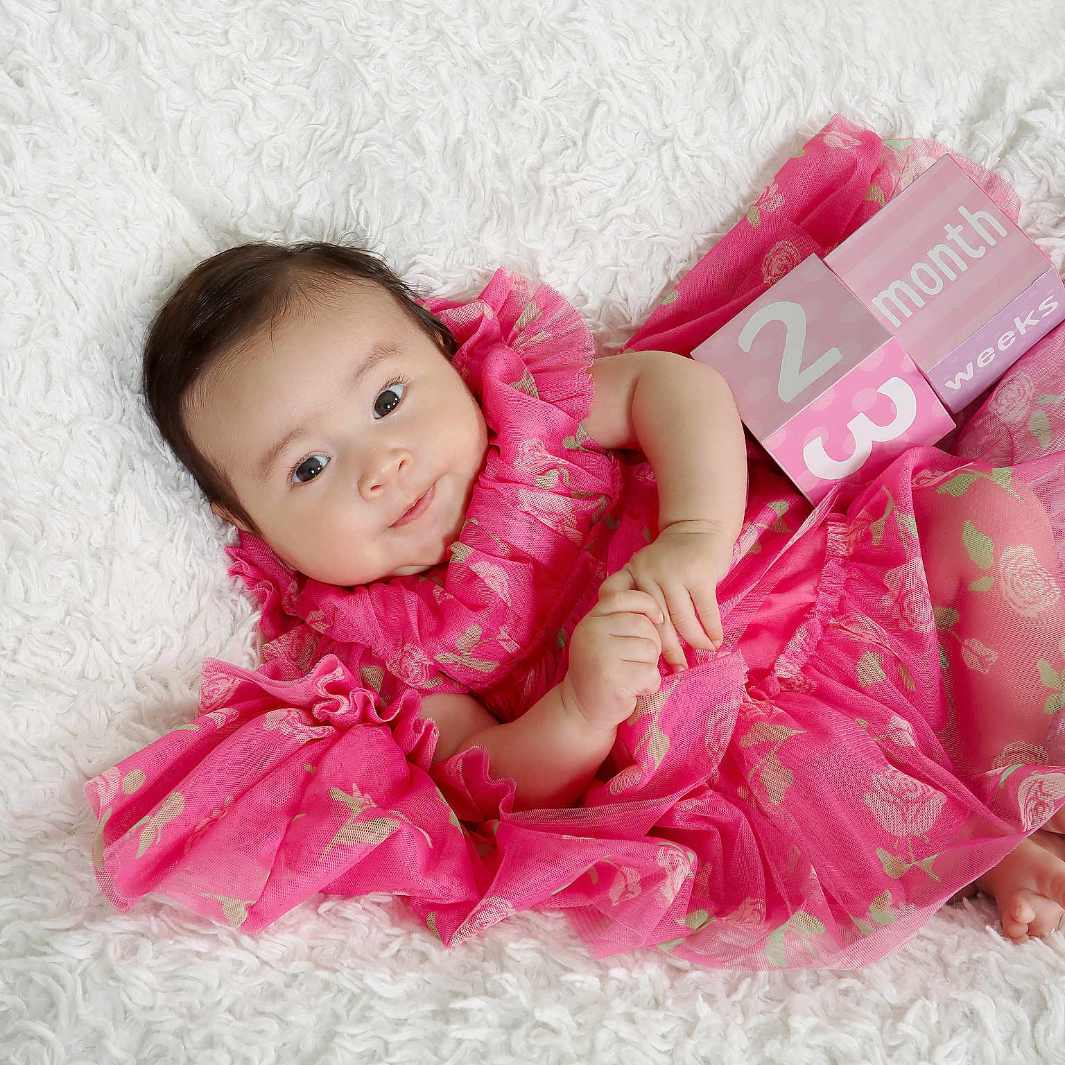 Isabella is registered to the contest to win money with this photo: age_blocks, baby, blocks, child, cute, face, feet, floral_pattern, hands, indoors, infant, lying_down, milestone, newborn, pink_dress, portrait, smiling, soft_texture, toddler, white_background