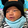 adorable, baby, blanket, blue_bib, child, close_up, cute, face, hat, indoor, infant, knit_hat, newborn, patterned_blanket, pom_poms, resting, soft_texture, striped_clothing, warm_clothing, young