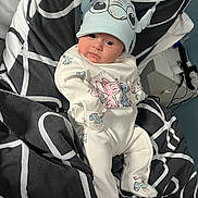 Alessia is registered to the contest to win money with this photo: baby, infant, child, hat, clothing, blanket, pattern, bedroom, indoor, person, cute, lying_down, soft_lighting, cartoon, footed_pajamas, sleepwear, face, expression, cozy, comfort