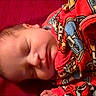 baby, infant, sleeping, portrait, close_up, face, closed_eyes, blanket, red_blanket, bedding, cozy, indoors, lying_down, peaceful, newborn, head, child, colorful, patterned_fabric, photography
