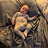 baby, sleeping, infant, child, bed, bedroom, pillow, blanket, bedsheets, onesie, clothing, pacifier, remote_control, portrait, indoors, furniture, relaxed, peaceful, nap, cozy