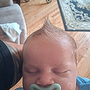 Noah is registered to the contest to win money with this photo: baby, infant, sleeping, pacifier, portrait, close_up, face, head, hair, spiky_hair, blue_clothing, indoors, home, wooden_floor, rug, chair, adult_arm, cozy, peaceful, photography