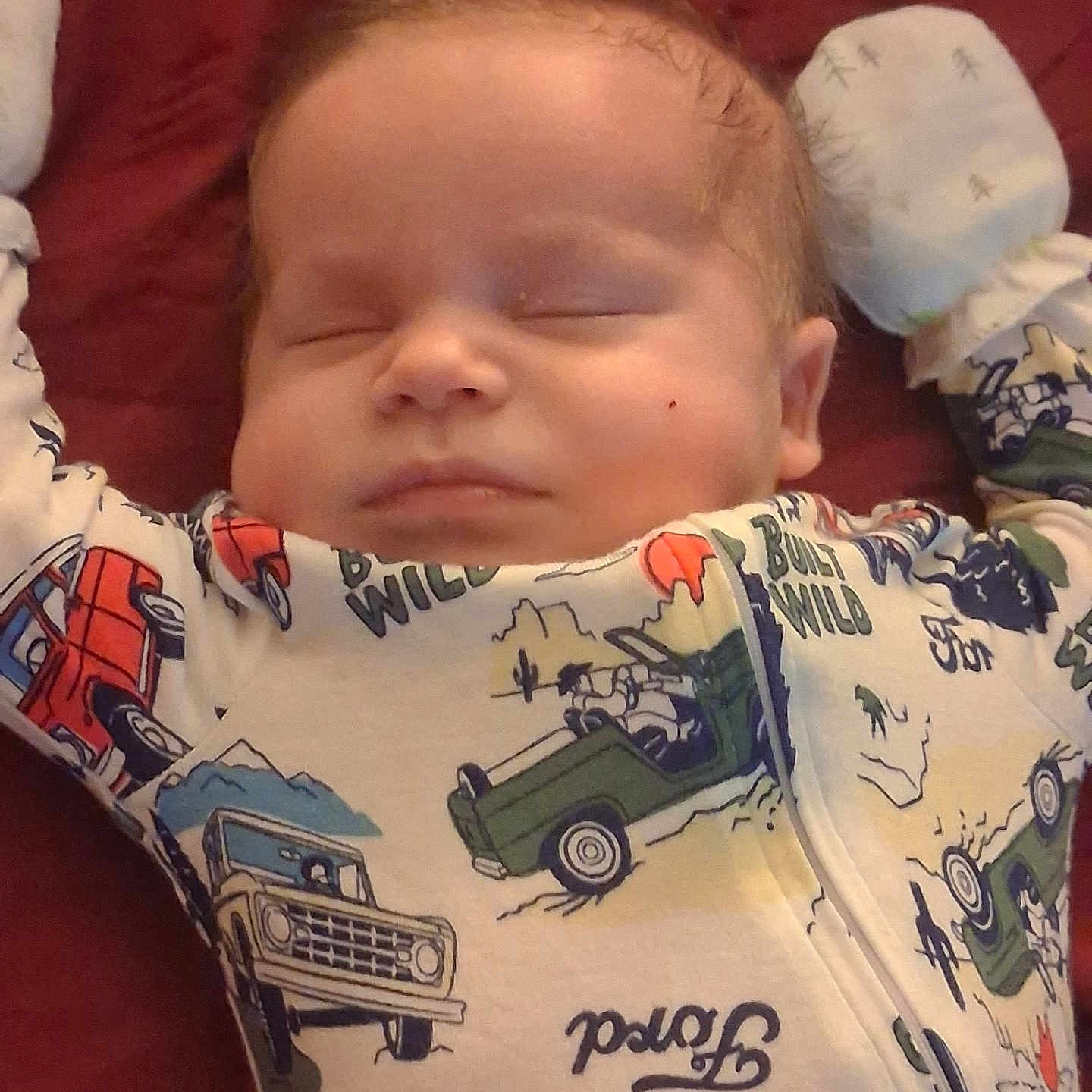 Noah joined the competition — help win amazing prizes! baby, infant, sleeping, child, portrait, face, closed_eyes, peaceful, cozy, blanket, onesie, clothing, vehicle_pattern, toy_cars, red_bedding, pillow, indoors, close_up, resting, cute