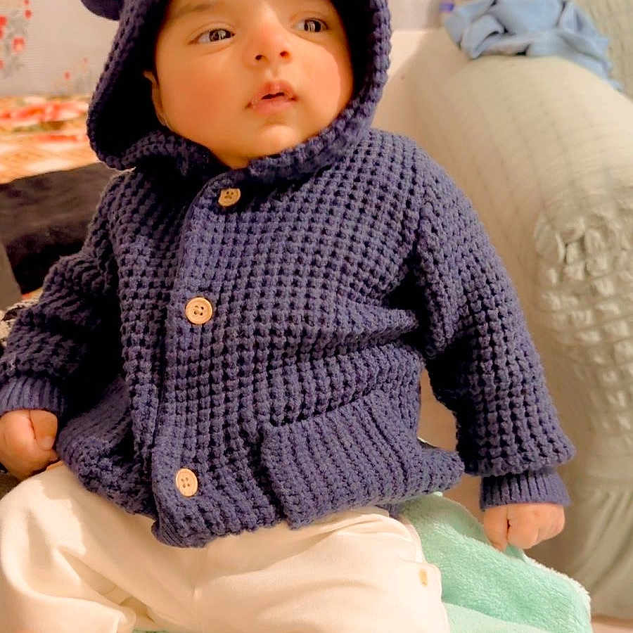 Shubh is registered to the contest to win money with this photo: baby, blanket, child, couch, cozy, curious_expression, cute, furniture, home, hood_with_ears, indoor, infant, knitted_hoodie, navy_blue, plush_toy, seated, socks, soft_toys, warm_clothing, white_pants