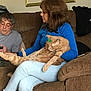 Archie is registered to the contest to win money with this photo: woman, man, cat, orange_tabby, sofa, living_room, blue_sweater, light_jeans, pink_socks, phone, brown_sofa, framed_painting, feather, relaxed, indoor, casual, home, seated, pet, couch