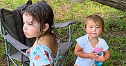 Delaney joined the competition — help win amazing prizes! toddler, child, outdoor, nature, grass, tree_branch, camping_chair, water_bottle, swimsuit, barefoot, playful, summer, greenery, two_children, curly_hair, short_hair, happy, exploring, daylight, casual