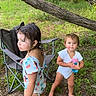toddler, child, outdoor, nature, grass, tree_branch, camping_chair, water_bottle, swimsuit, barefoot, playful, summer, greenery, two_children, curly_hair, short_hair, happy, exploring, daylight, casual
