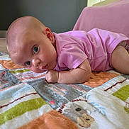 Zoey is registered to the contest to win money with this photo: baby, blanket, carpet, child, clothing, colorful, curious, cute, eyes, face, floor, head, indoor, infant, lying_down, pattern, person, pink_onesie, skin, toddler