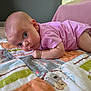 baby, blanket, carpet, child, clothing, colorful, curious, cute, eyes, face, floor, head, indoor, infant, lying_down, pattern, person, pink_onesie, skin, toddler
