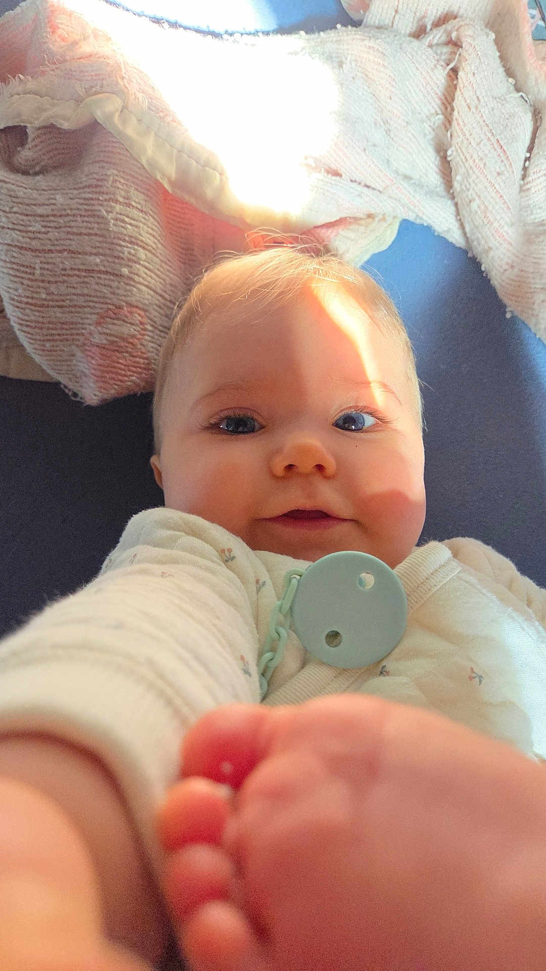 Maïna a rejoint le concours — aidez-le/la à gagner de superbes lots ! baby, infant, portrait, close_up, smile, toes, pacifier, pacifier_clip, blanket, sunlight, indoors, hand, foot, eyes, cheeks, onesie, soft_texture, blanket_pattern, adorable, face