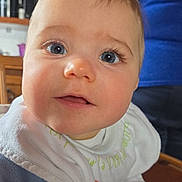 Maïna a rejoint le concours — aidez-le/la à gagner de superbes lots ! baby, infant, close_up, face, blue_eyes, long_eyelashes, bib, pacifier_clip, toy, blanket, clothing, chubby_cheeks, curious_gaze, indoor, kitchen_background, wooden_furniture, shelf, adult_torso, portrait, smile