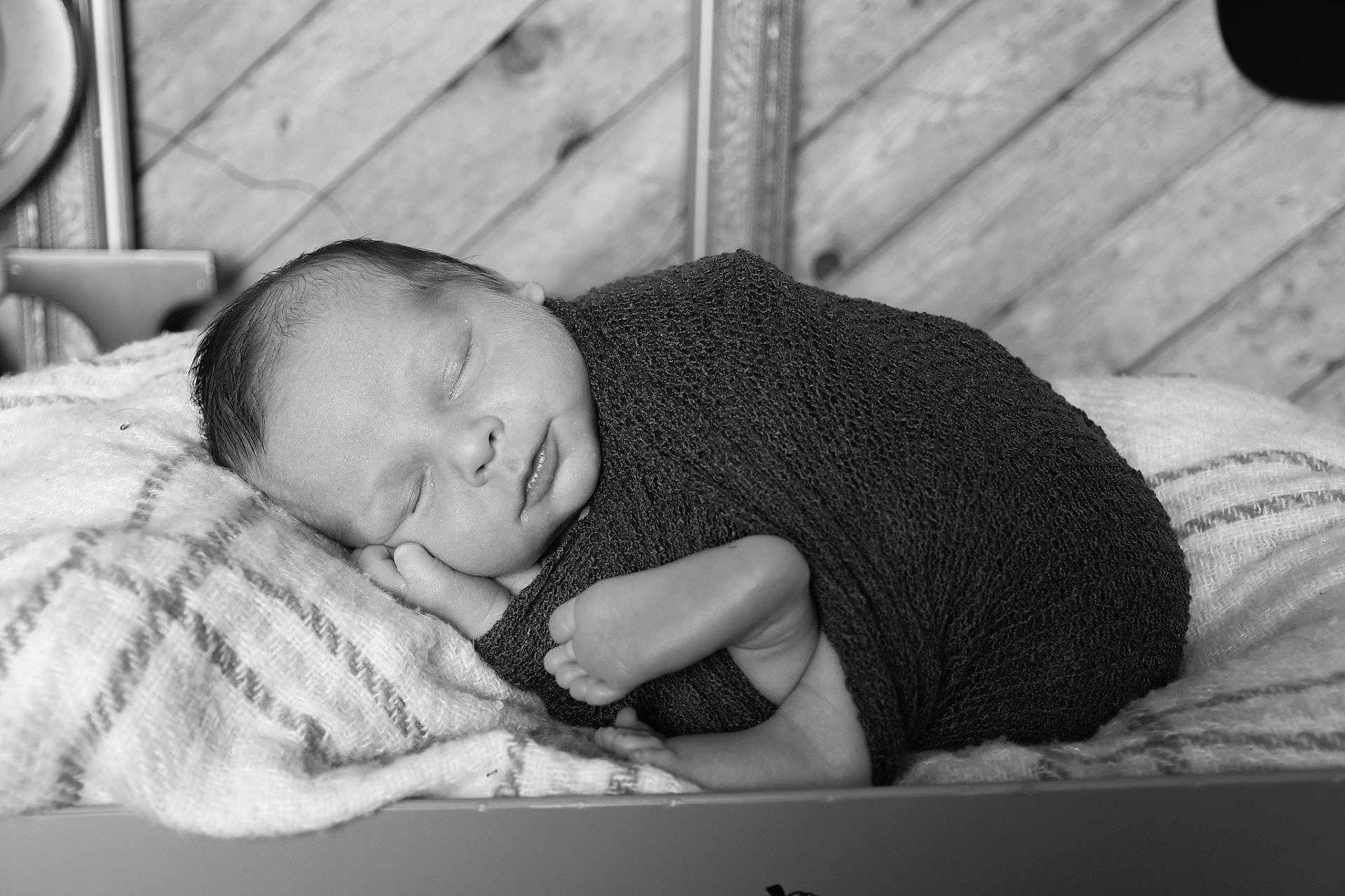 Maddux is registered to the contest to win money with this photo: newborn, baby, sleeping, wrapped, blanket, black_and_white, portrait, infant, peaceful, soft, texture, wooden_background, cushion, cozy, closeup, face, foot, hand, resting, peace