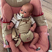 Liam a rejoint le concours — aidez-le/la à gagner de superbes lots ! baby, baby_accessory, baby_seat, beige, child, clothing, comfort, cushion, cute, indoor, infant, overalls, pacifier, person, pink, relaxing, seated, small, white_shirt, wooden_floor