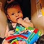 baby, infant, car_seat, headband, toy, soft_book, fingers, foot, warning_label, seatbelt, child, cute, indoor, closeup, expression, polka_dot_clothing, colorful, comfort, seat, person