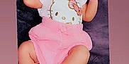 Lydia is registered to the contest to win money with this photo: adorable, baby, child, clothing, cushion, cute, dark_background, face, hello_kitty, indoors, infant, lying_down, person, pink_skirt, playful, relaxed, skin, smiling, tongue_out, white_top