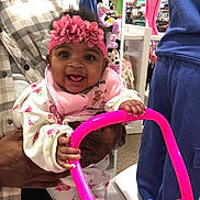 Tori joined the competition — help win amazing prizes! baby, child, infant, smiling, pink_headband, bib, toy, shopping_store, mannequin, clothing, adult_hand, joyful, portrait, indoor, person, happy, cute, playful, holding, bright_colors
