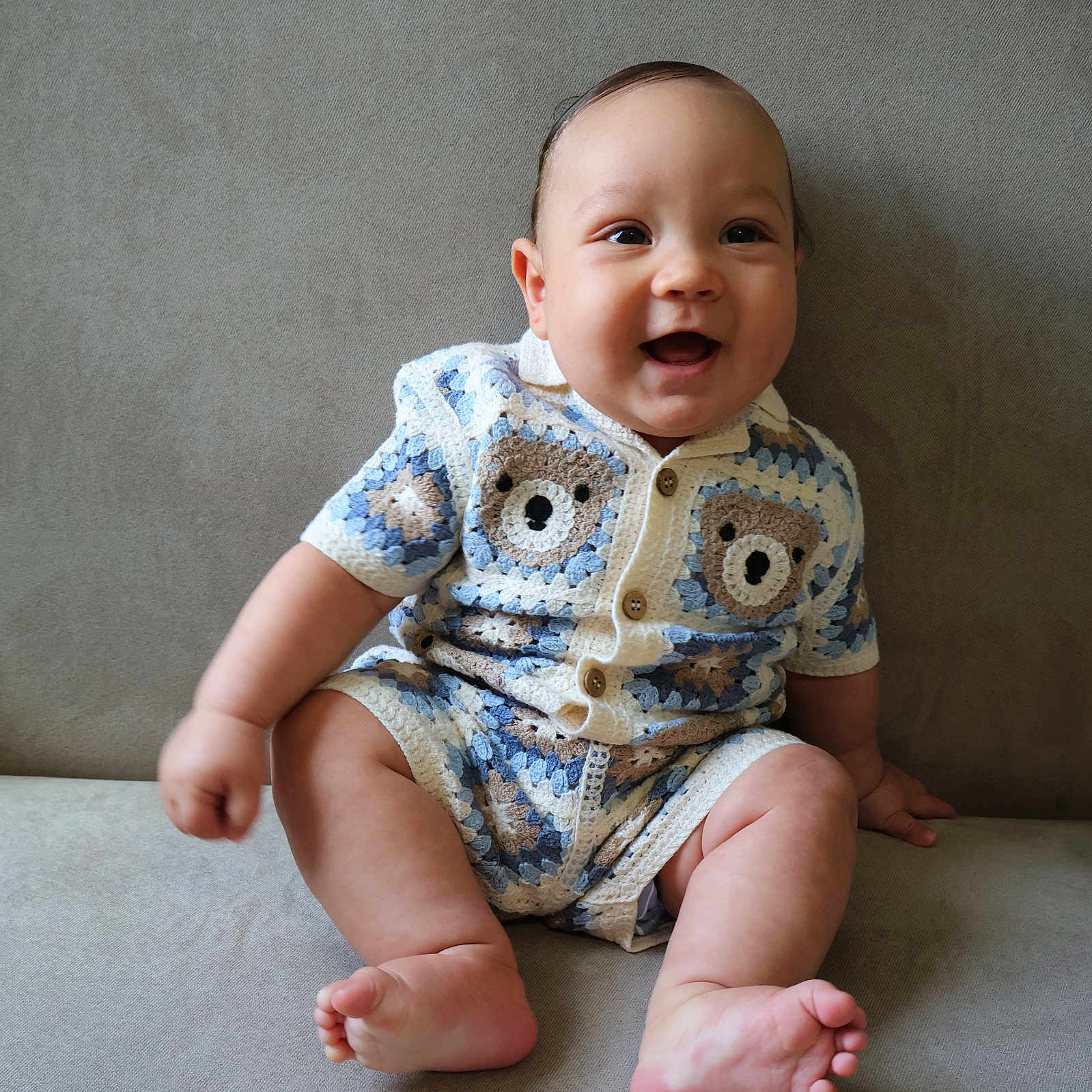 Luka joined the competition — help win amazing prizes! baby, child, smiling, sitting, indoors, couch, crocheted_clothing, bear_pattern, cute, happy, plump, short_sleeves, foot, hand, face, person, infant, portrait, casual, neutral_background