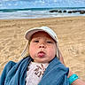 baby, child, face, tongue, hat, blue_blanket, beach, sand, ocean, sky, clouds, person, cute, infant, summer, outdoor, playful, portrait, headwear, expression