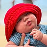 Luka is registered to the contest to win money with this photo: baby, child, red_hat, striped_clothing, hand, puckered_lips, cute, chubby_cheeks, portrait, outdoor, beach, blurred_background, infant, person, skin, headwear, casual_wear, closeup, expression, holding