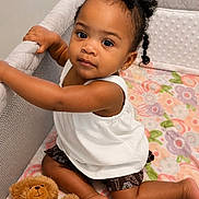 Harlei joined the competition — help win amazing prizes! toddler, child, baby, curly_hair, playpen, blanket, teddy_bear, toy, indoor, cute, portrait, sitting, clothing, white_top, brown_shorts, skin, person, infant, earrings, floor