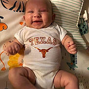 Oakley is registered to the contest to win money with this photo: baby, smiling, onesie, texas, infant, lying_down, blanket, animal_print, cute, chubby_arms, chubby_legs, happy, indoor, child, person, head, face, pillow, soft_toys, cozy