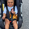 toddler, child, smile, stroller, colorful_hair_clips, baby, footwear, sandals, clothing, happy, person, outdoor, seatbelt, black_stroller, skin, hand, legs, road, photography, cute