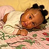 baby, child, infant, face, puffs_hairstyle, quilt, floral_pattern, bedspread, indoor, cute, smile, lying_down, curious, soft_lighting, skin, clothing, sleeves, earrings, portrait, cozy