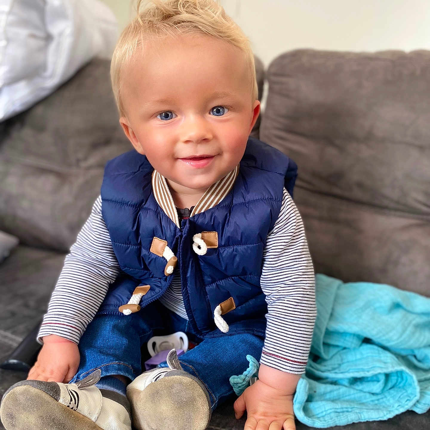 Nolan participe au concours pour gagner de l'argent avec cette photo : blanket, blonde_hair, blue_eyes, casual, child, couch, cozy, cute, face, hand, home, indoor, jeans, navy_vest, portrait, shoes, sitting, smiling, striped_shirt, toddler