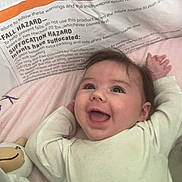 Shelby is registered to the contest to win money with this photo: baby, smiling, infant, crib, blanket, stuffed_toy, happy, face, child, soft_toys, clothing, lying_down, cute, indoors, head, person, young_child, baby_girl, white_clothing, cozy