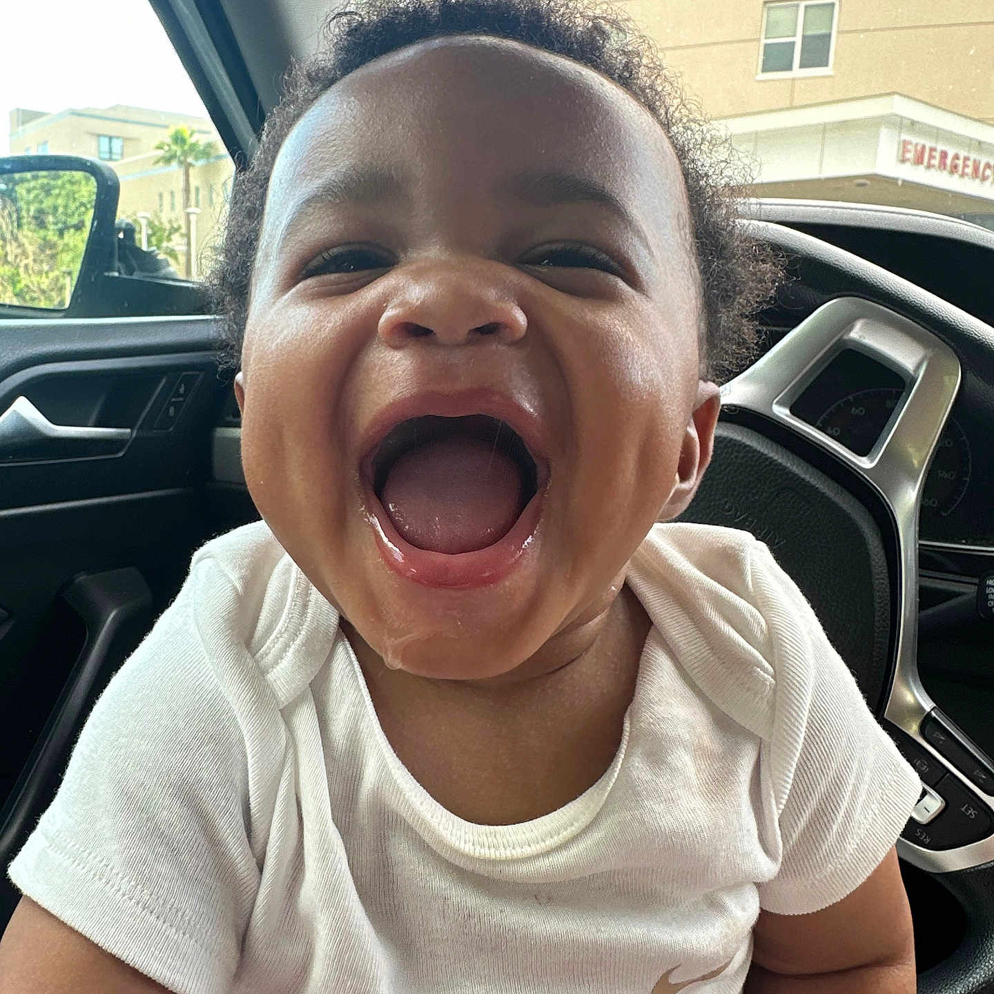 Zachary joined the competition — help win amazing prizes! toddler, child, smiling, laughing, car_interior, white_shirt, curly_hair, happy, portrait, face, mouth_open, seat, window, steering_wheel, daylight, building, emergency_sign, joy, cute, person