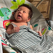 Tony joined the competition — help win amazing prizes! baby, infant, striped_blanket, baby_bouncer, colorful, animal_prints, curious, indoor, wooden_cabinet, hand, face, expression, comfort, child, person, seat, toy, smiling, young, resting