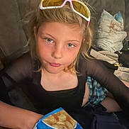 Gracelyn joined the competition — help win amazing prizes! child, blonde_hair, sunglasses, chips, couch, pillow, casual_clothing, indoor, snack, blue_bag, person, young, sitting, face, looking_at_camera, hand, relaxed, home, comfortable, expression