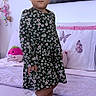 Salome is registered to the contest to win money with this photo: child, girl, toddler, portrait, standing, smiling, floral_dress, dress, sneakers, white_shoes, socks, bedroom, bed, pink_bedding, stuffed_toy, pillow, cityscape, wall_art, indoor, fashion_pose