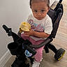 child, toddler, tricycle, plush_toy, sitting, indoors, wood_floor, white_wall, pink_pants, white_shirt, sneakers, braided_hair, portrait, vehicle, toy, baby, wheel, handlebar, home, cute