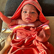 Naylani joined the competition — help win amazing prizes! baby, infant, towel, orange, hooded_towel, face, wide_eyes, hand, tattoo, skin, blanket, fabric, indoor, couch, light, rainbow_reflection, cute, portrait, newborn, expression