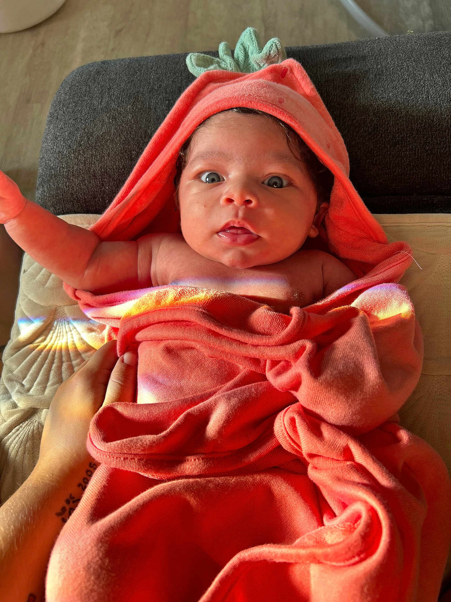 Naylani joined the competition — help win amazing prizes! baby, infant, towel, orange, hooded_towel, face, wide_eyes, hand, tattoo, skin, blanket, fabric, indoor, couch, light, rainbow_reflection, cute, portrait, newborn, expression