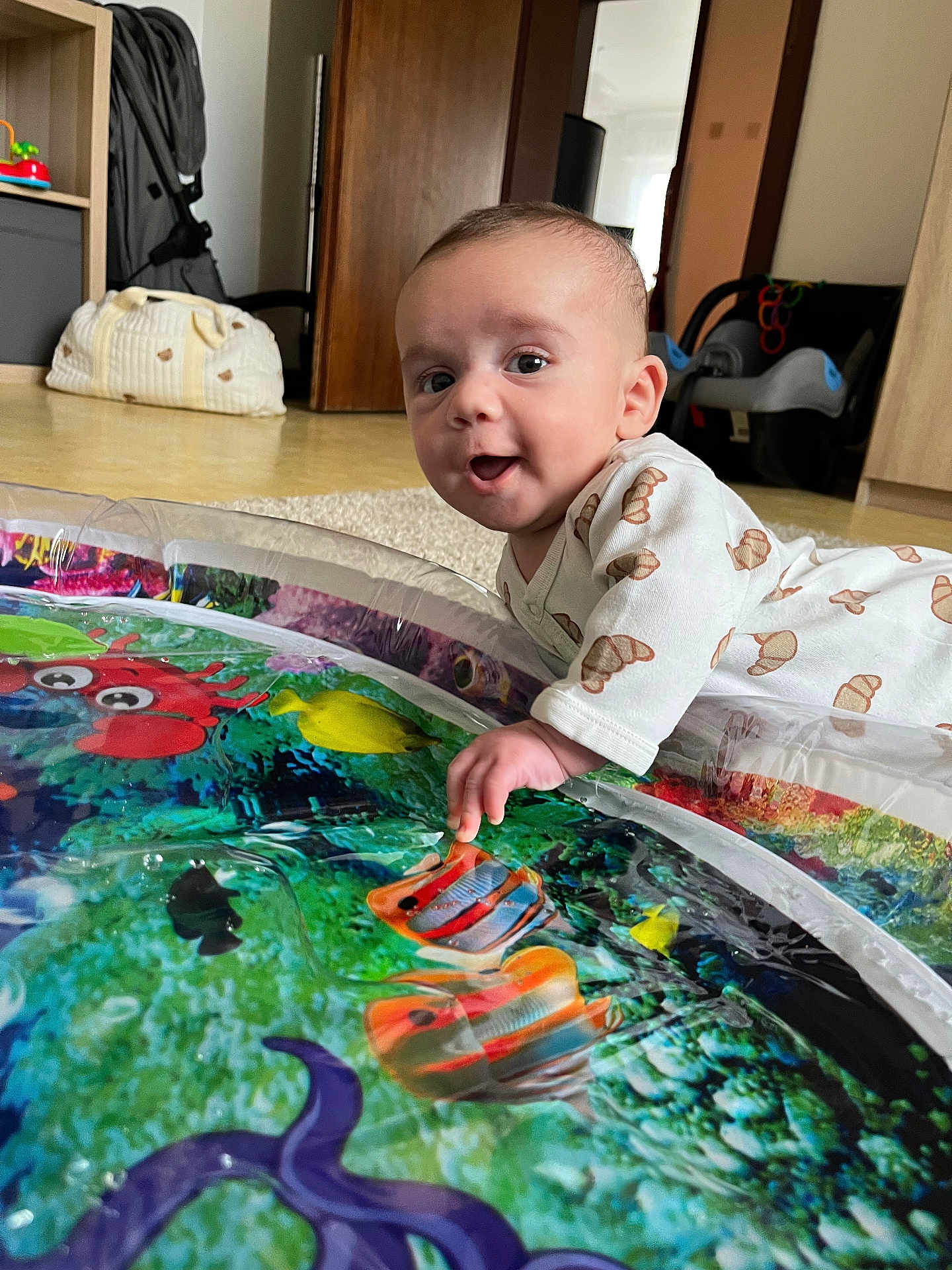 Basil participe au concours pour gagner de l'argent avec cette photo : baby, infant, tummy_time, play_mat, water_play_mat, smiling, hand, face, eyes, onesie, croissant_pattern, indoor, carpet, car_seat, stroller, toy, colorful, floor, mirror, home