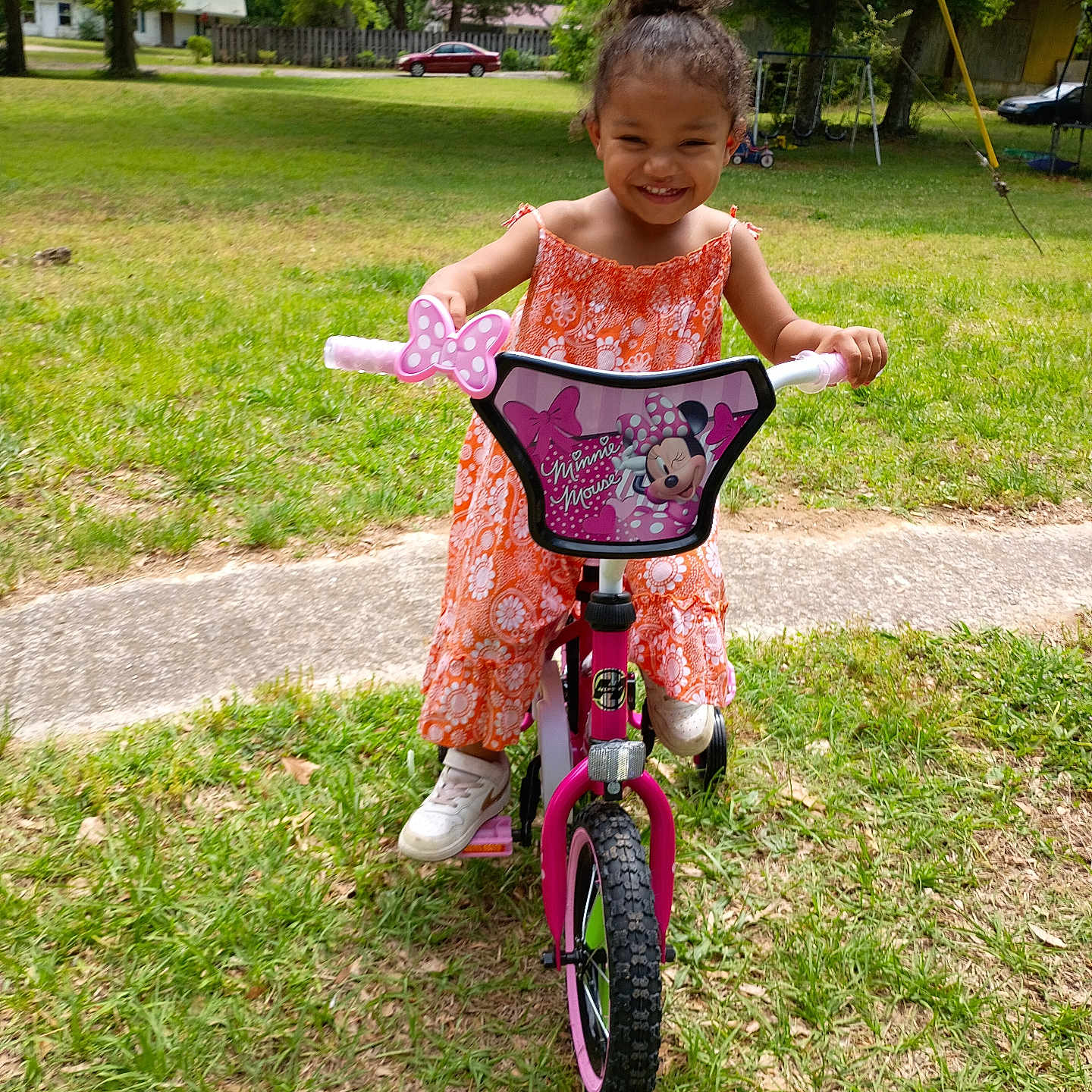 Khloe is registered to the contest to win money with this photo: child, girl, bicycle, pink_bike, orange_dress, smiling, outdoor, grass, trees, sunny_day, toy, play, happy, cute, young, person, footwear, park, nature, recreation